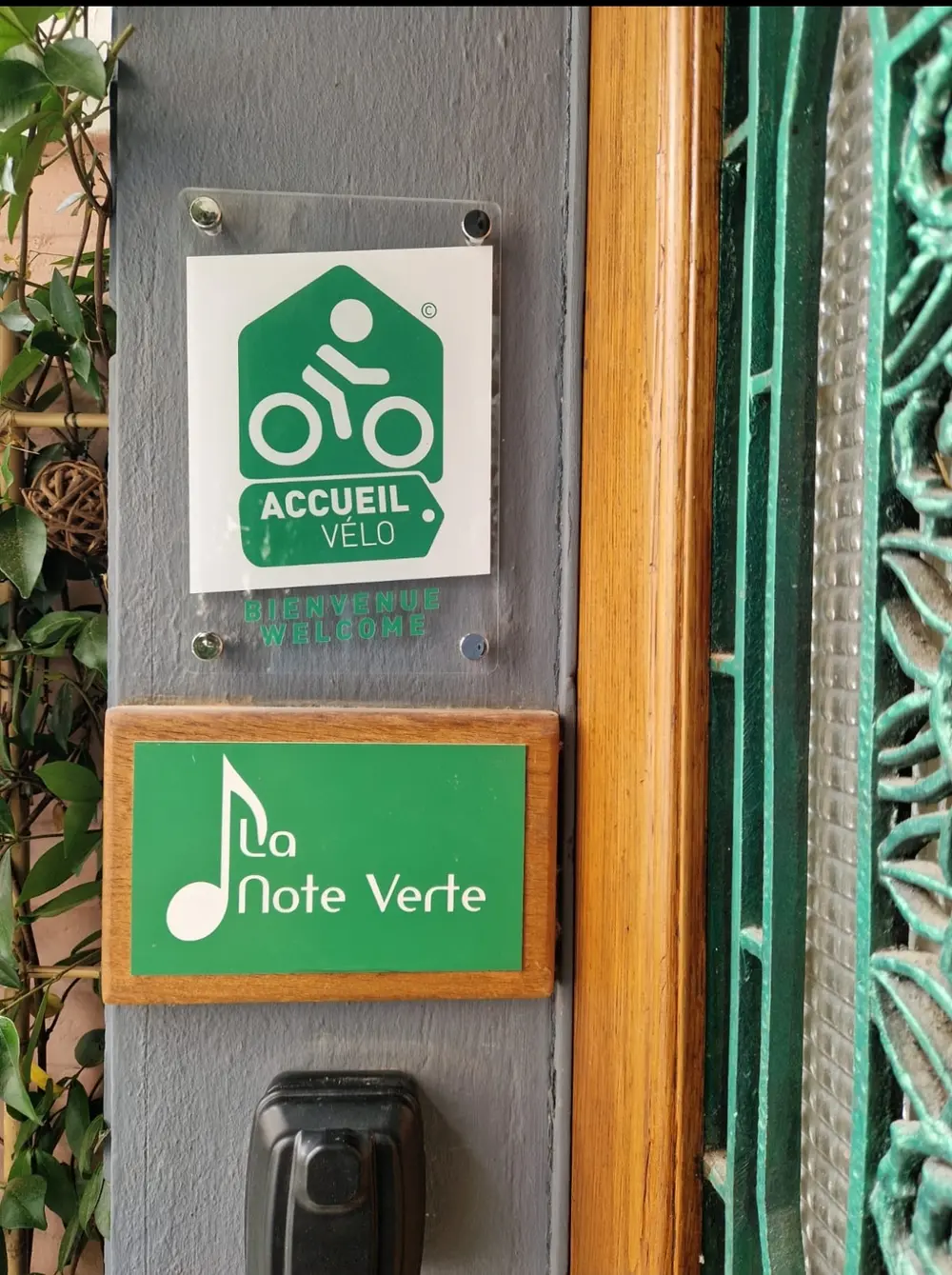 La plaque Accueil Vélo « Bienvenue, Welcome » et l'enseigne La Note Verte à l'entrée du gîte