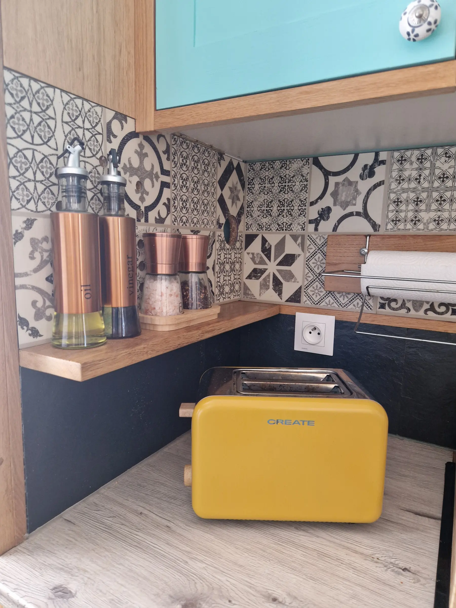 Coin cuisine : grille-pain jaune, huilier, moulins à sel et poivre devant une crédence en carreaux de ciment