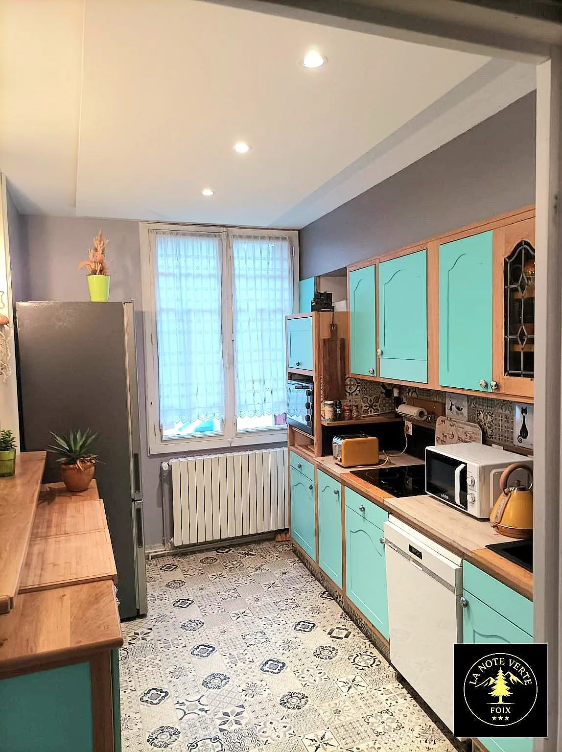 La cuisine équipée : meubles turquoise, crédence en carreaux de ciment, plantes suspendues
