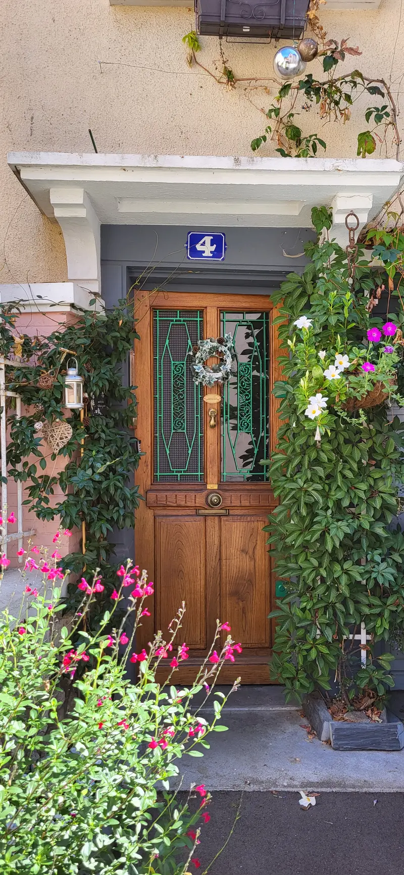 La porte d'entrée en chêne aux vitraux verts, encadrée de plantes grimpantes et de fleurs